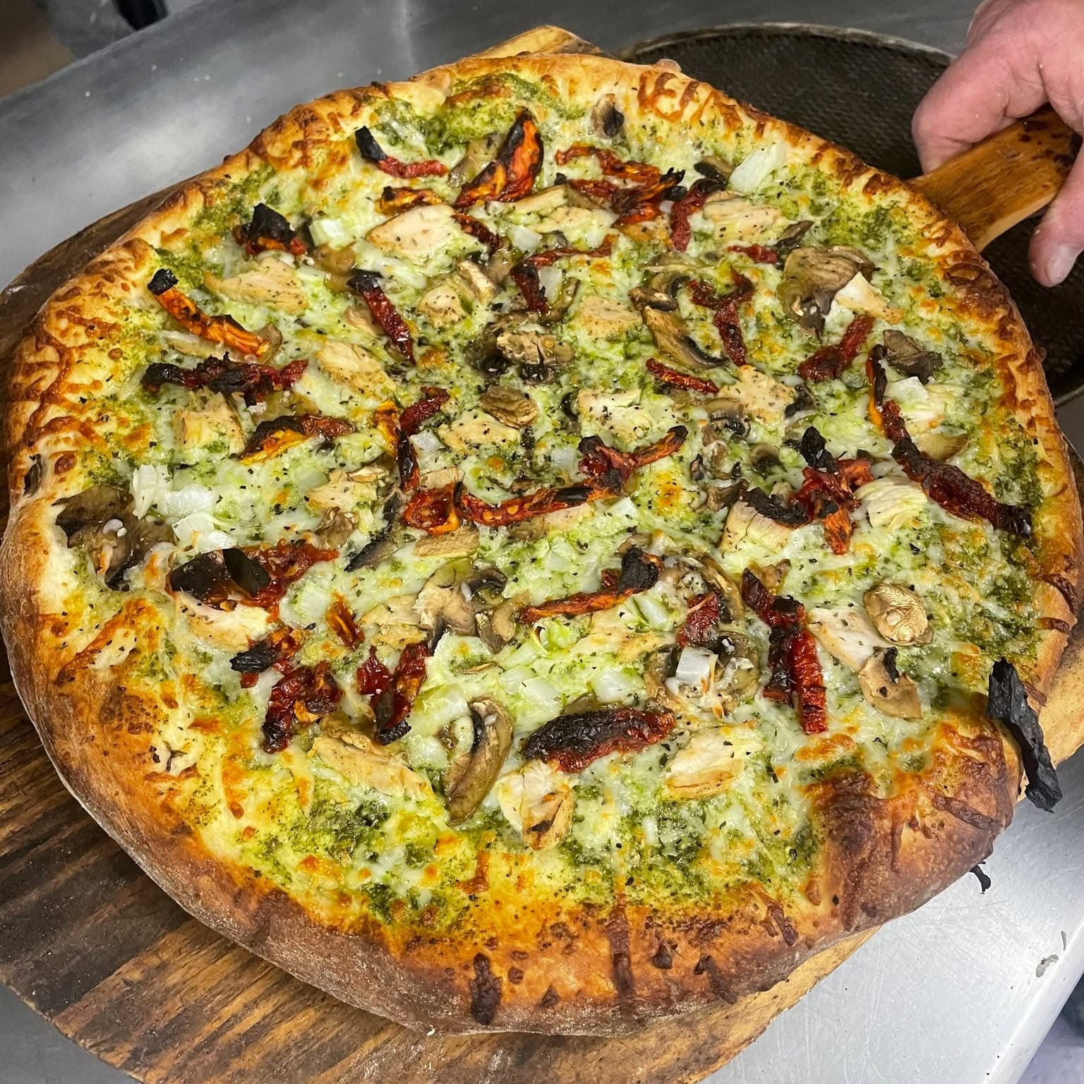 A fresh pesto pizza on a wooden peel